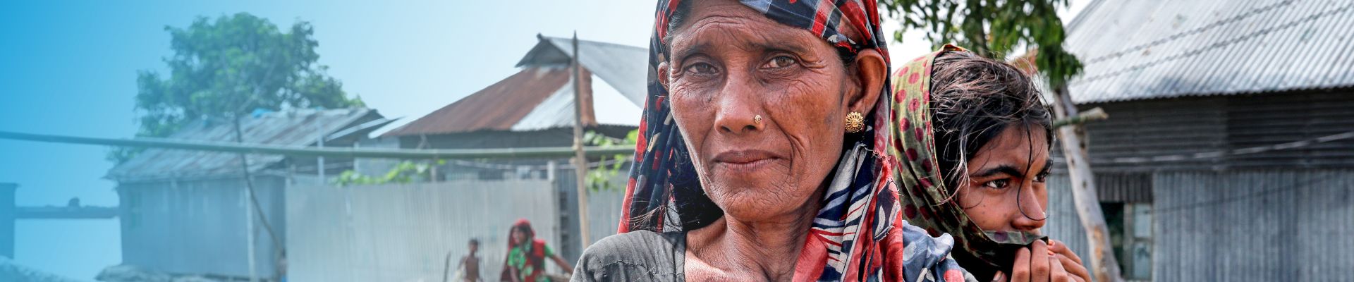 Frauen in der Klimakrise helfen. Frau und Mädchen in Bangladesch stehen in von Flut zerstörten Trümmern