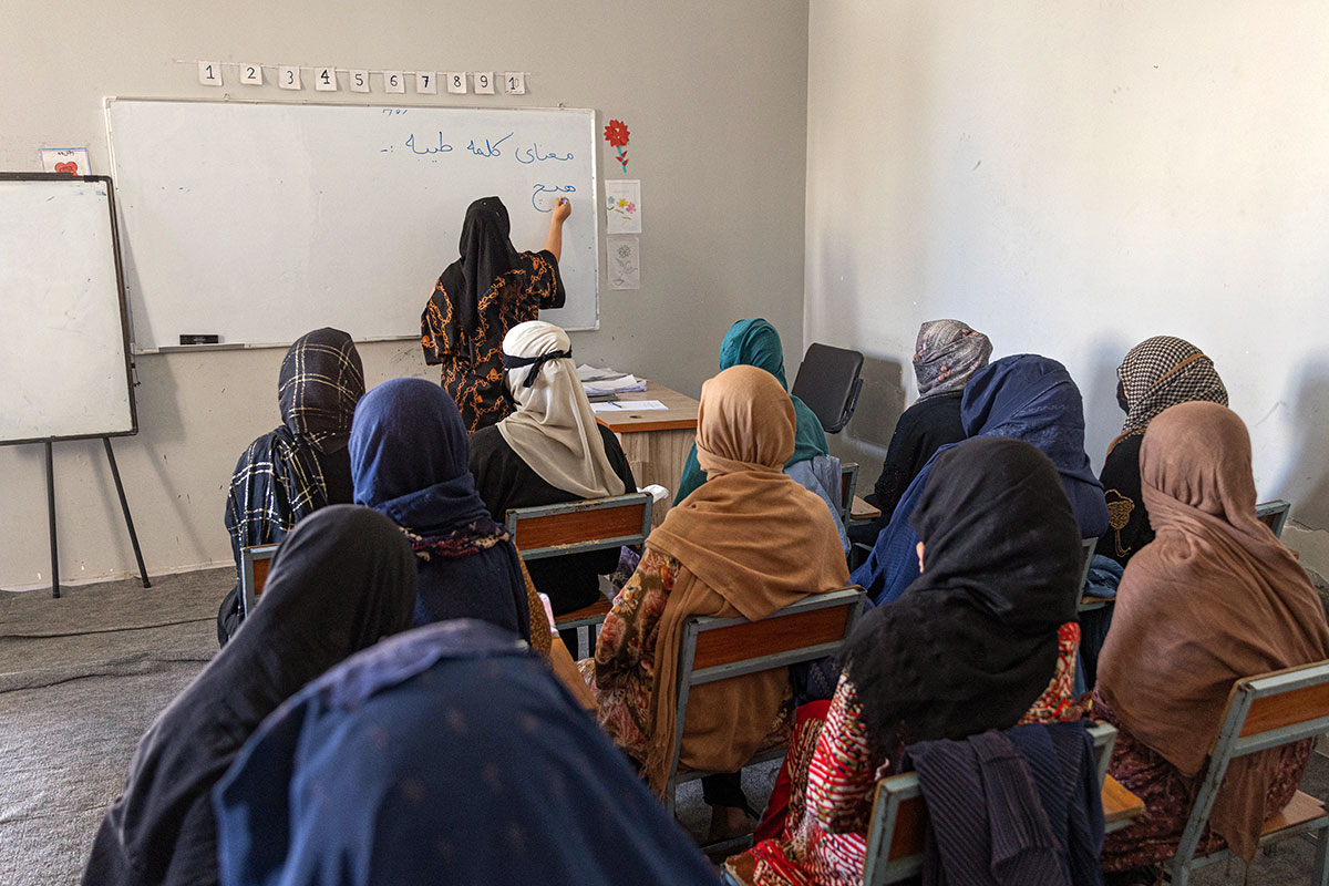 Frau schreibt an ein Whiteboard in einer Klasse mit weiteren Frauen mit Schleier - Afghanistan