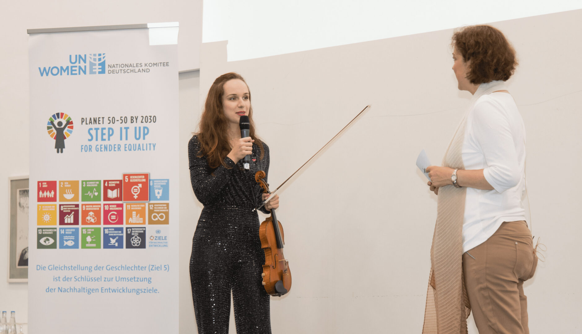 Violinistin und Initiatorin von Music for our Planet Lea Brückner hält ihre Geige in der Hand und hält eine Rede gegenüberstehend Bürgermeisterin Dr. Ursula Sautter. Credit: UN Women Deutschland/Ortrud Ladleif