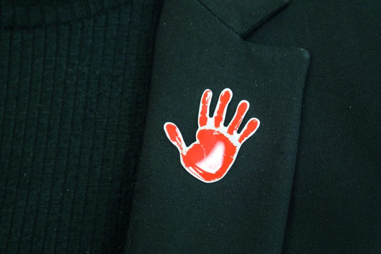 Orange the World Pin - Oranger Handabdruck als Pin an schwarzer Kleidung