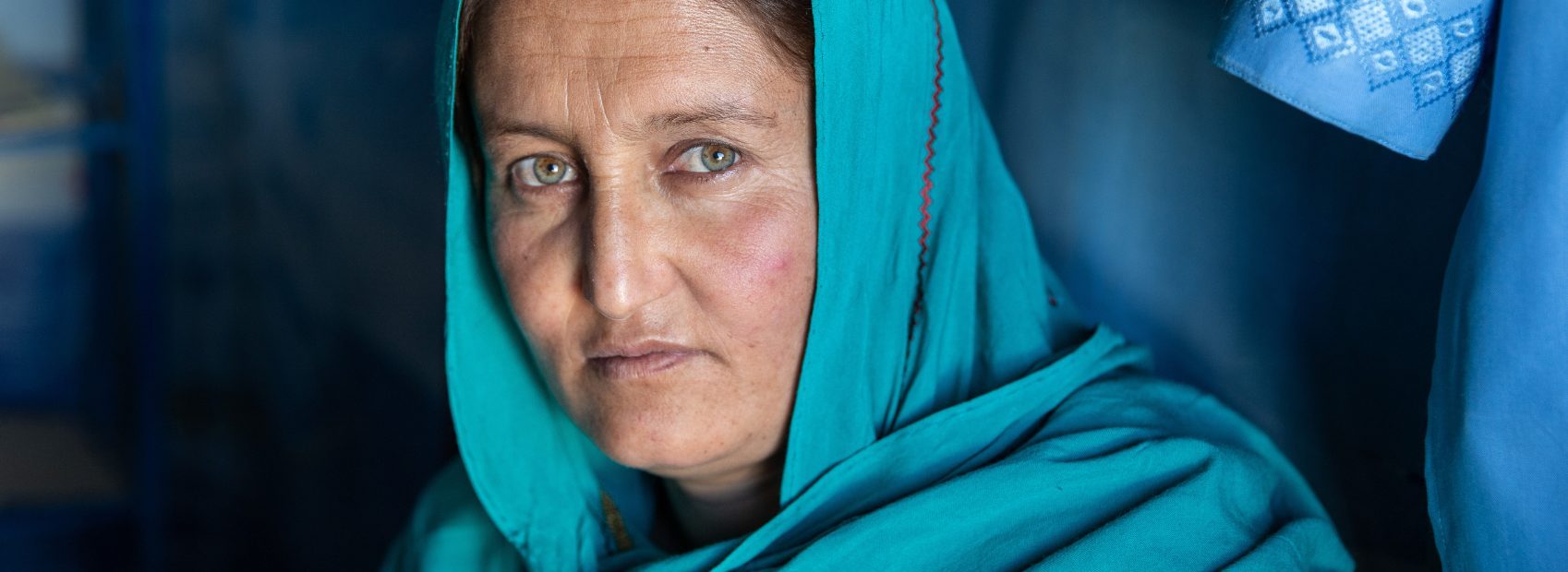Afghanische Frau mit blauem Kopftuch schaut in die Kamera - UN Women hilft Frauen in Afghanistan