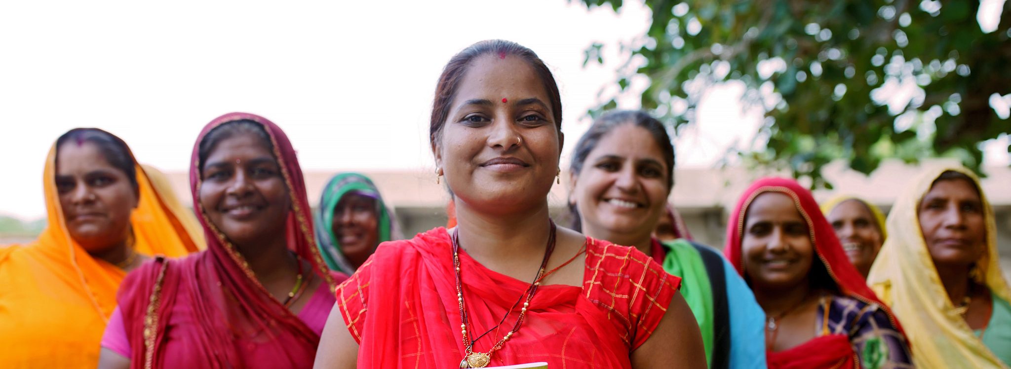 Indische Frauen in bunten Kleidern lächeln glücklich in die Kamera. Als UN Women Friend und regelmäßige Spender*in ermöglichen Sie Frauen weltweit die Hilfe zur Selbsthilfe.