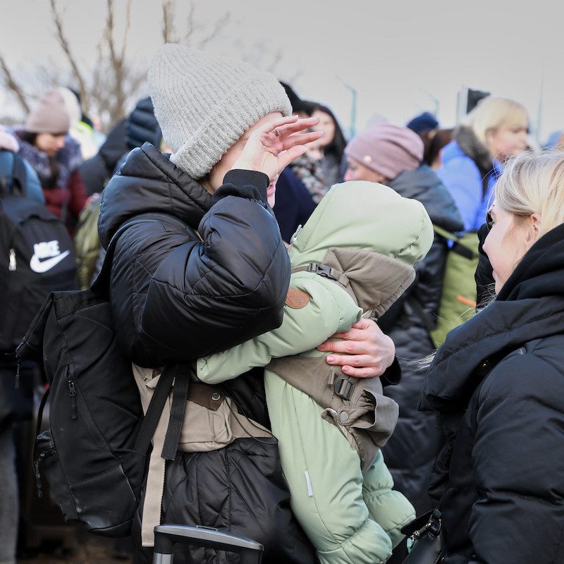 An der Grenze von der Ukraine zu Moldawien fliehen Menschen vor der russichen Invasion. Eine Frau verdeckt ihr Gesicht mit einer Hand und trägt ein Baby in der anderen.