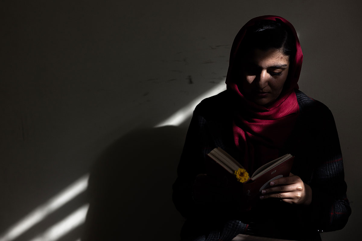 Afghanische Frau sitzt im Schatten und liest ein Buch - UN Women Deutschland Kampagne - In Frauen Investieren