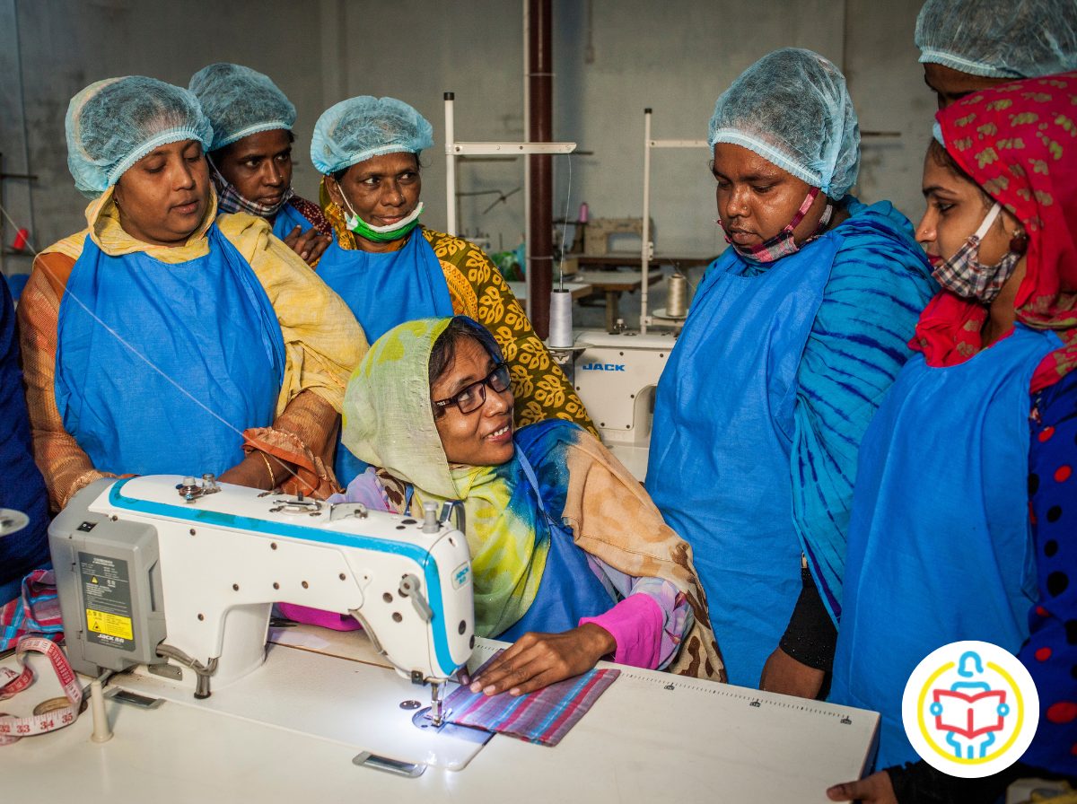 Eine Frau sitzt an der Nähmaschine und erklärt weiteren Frauen, wie diese funktioniert. UN Women - Bangladesch
