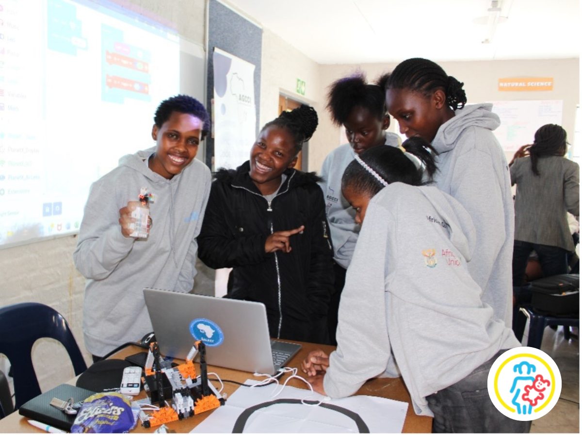 Eine Gruppe Mädchen steht vor einem Laptop. Zwei lächeln in die Kamera. African Girls Can Code Projekt
