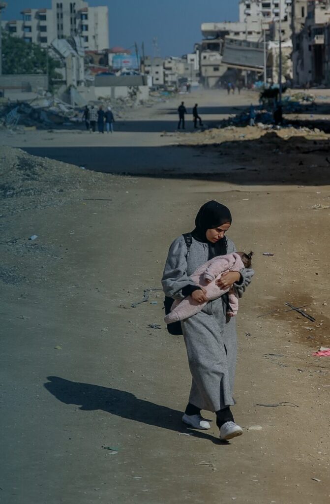 Frau läuft mit Baby im Arm inmitten von Bomben zerstörten Straßen