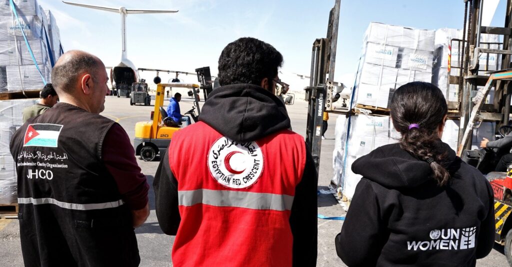3 Personen beobachten die Verladung von Nothilfepaketen am Flughafen - Nothilfe Gaza Israel - lebensrettende Hilfe für 15000 Frauen und Mädchen - UN Women Deutschland