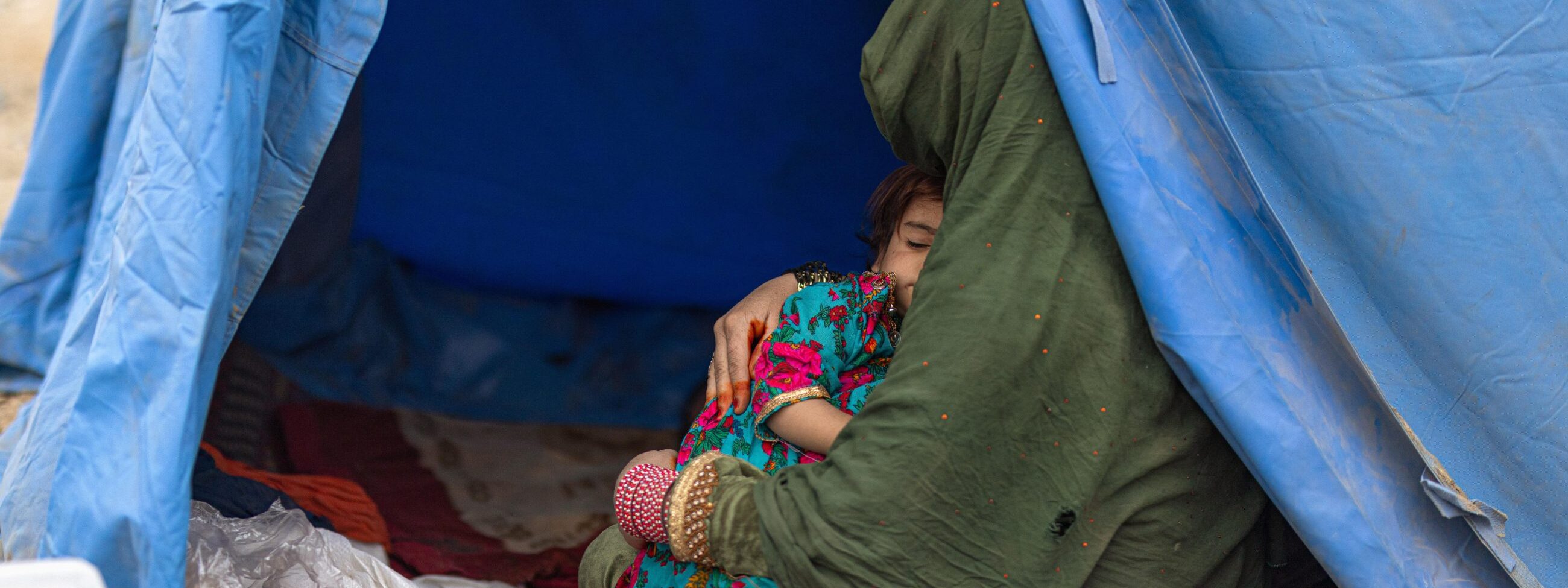 Afghanische Frau mit ihrer Tochter im Arm in einem blauen Zelt