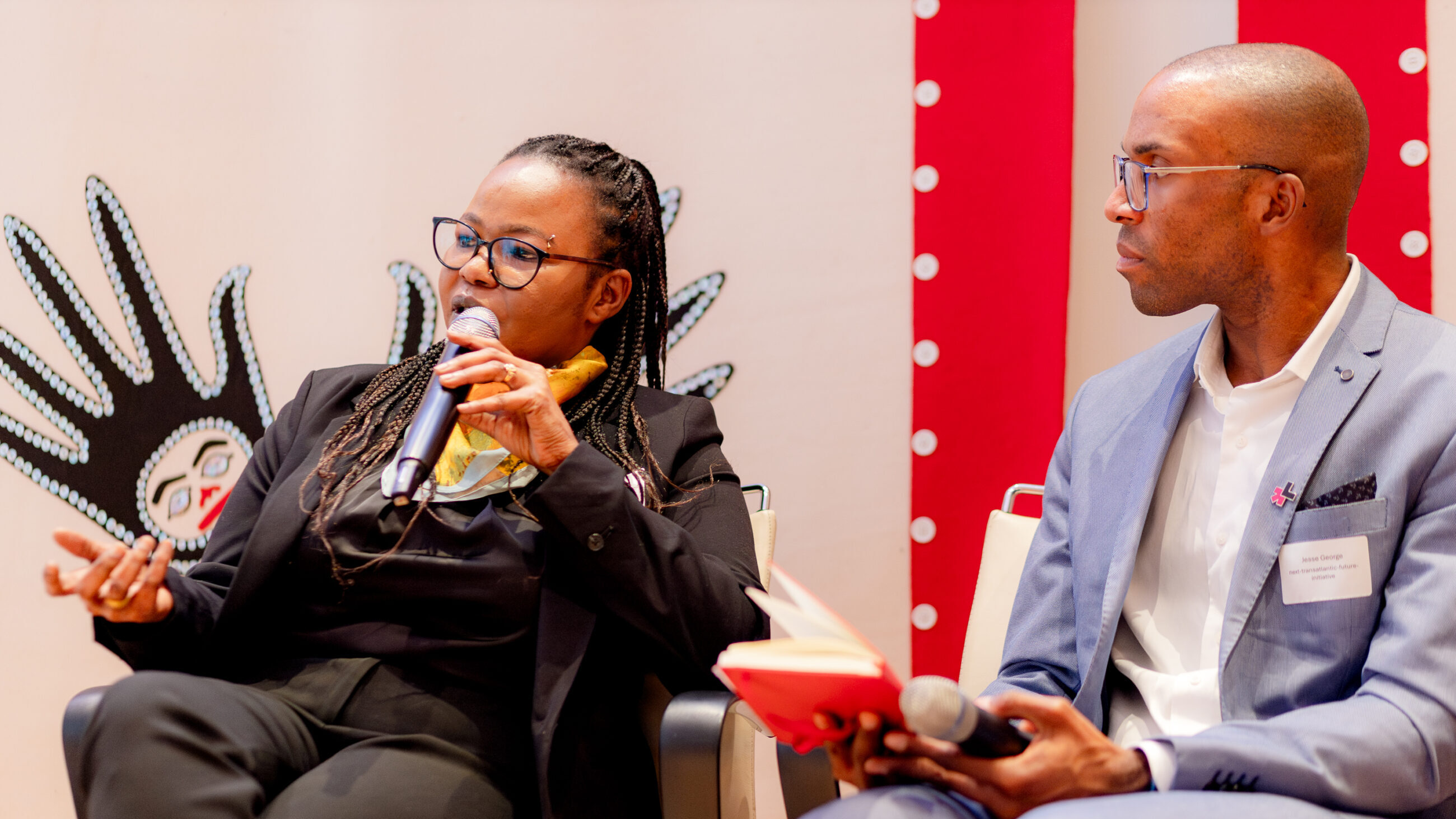 Mail Ali Shatta and Jesse George on the stage at the conference. Mai is speaking into her microphone.