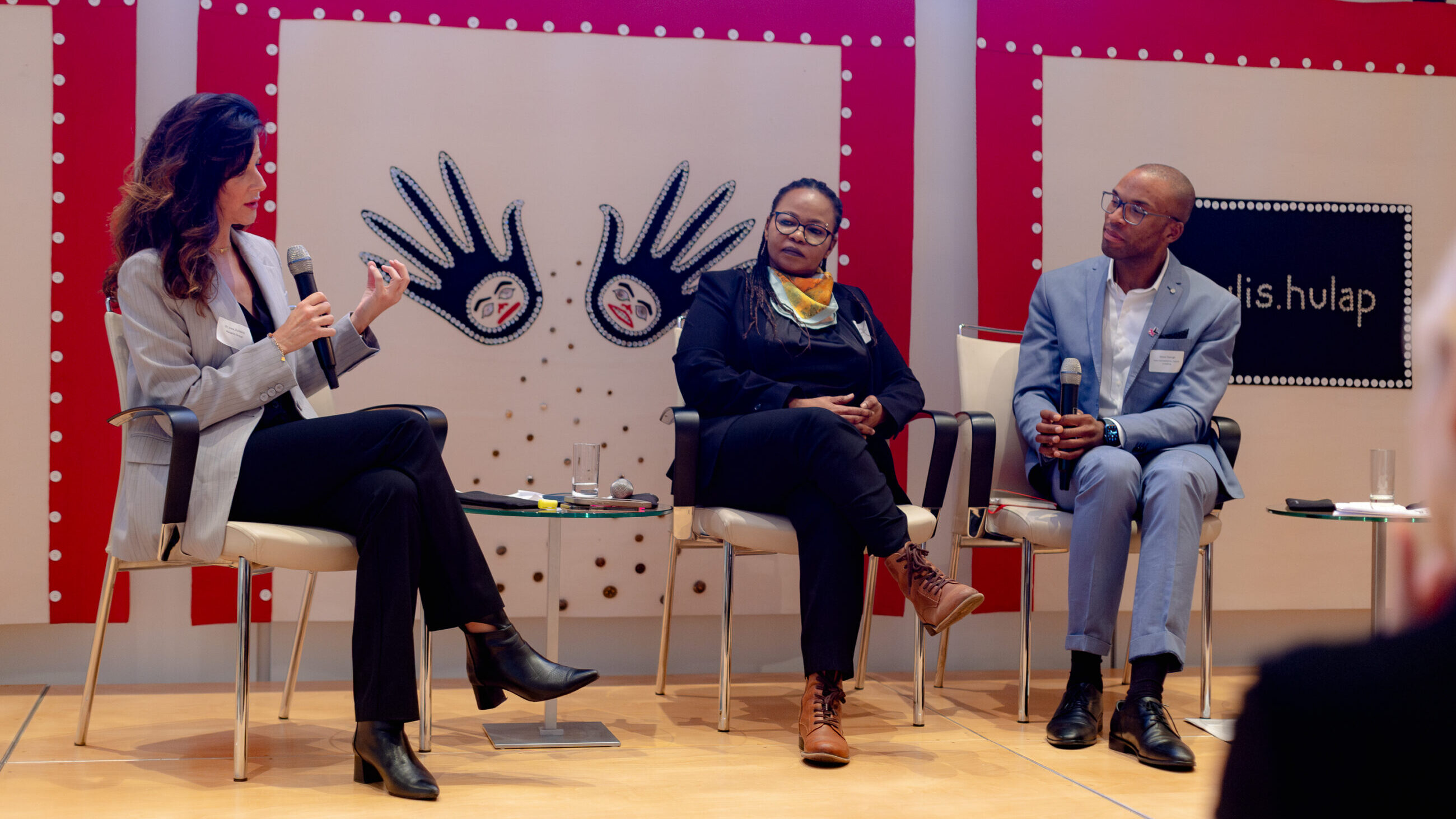 A participant from the audience is speaking on stage next to Mai Ali Shatta and Jesse George.