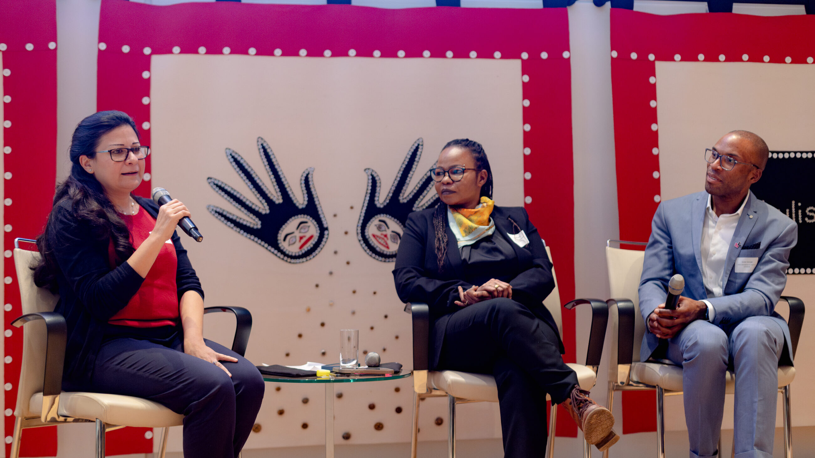 A participant from the audience is speaking on stage next to Mai Ali Shatta and Jesse George.