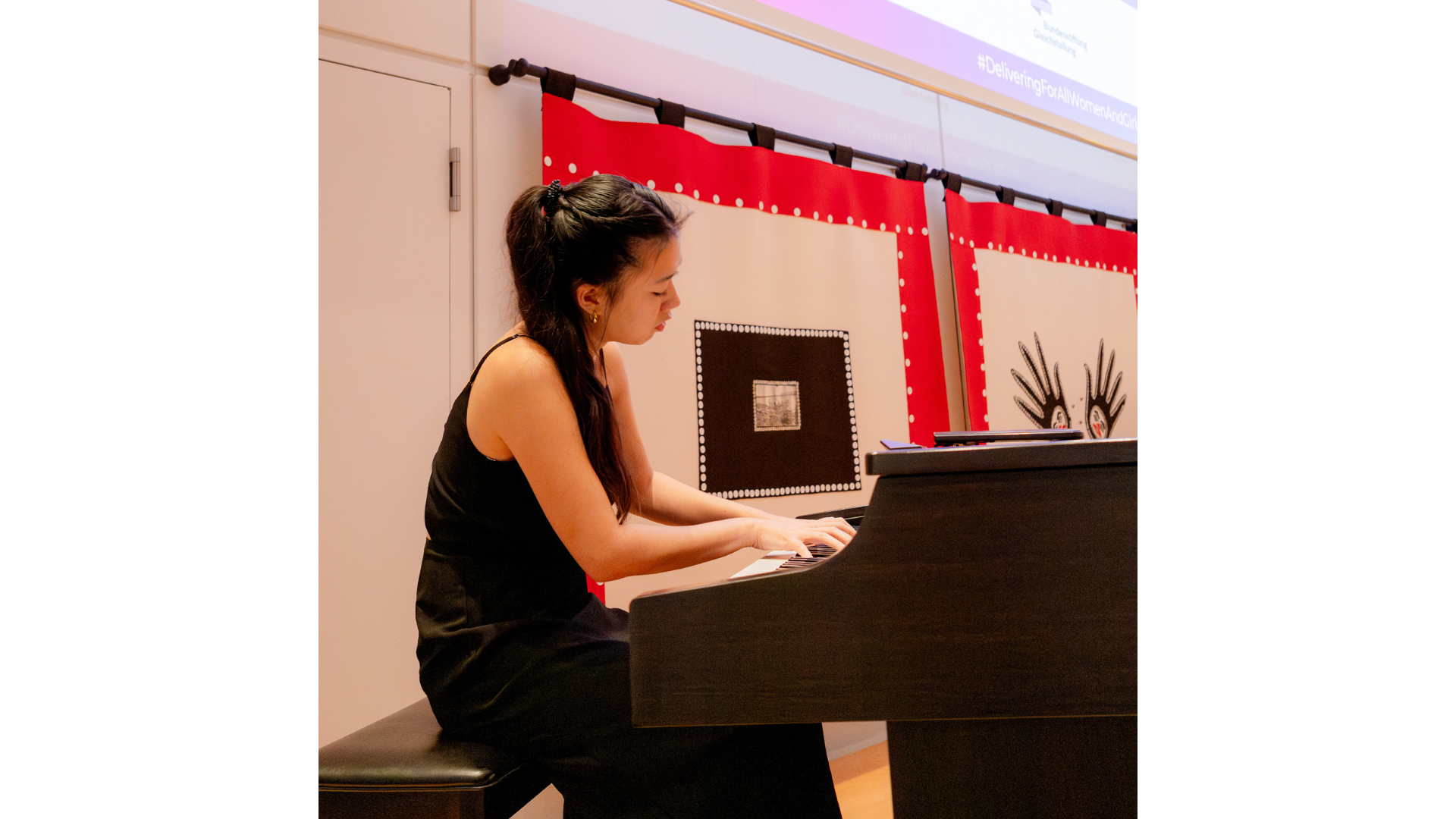 Caitlan Rinaldy at the piano on stage at the conference, playing two pieces.