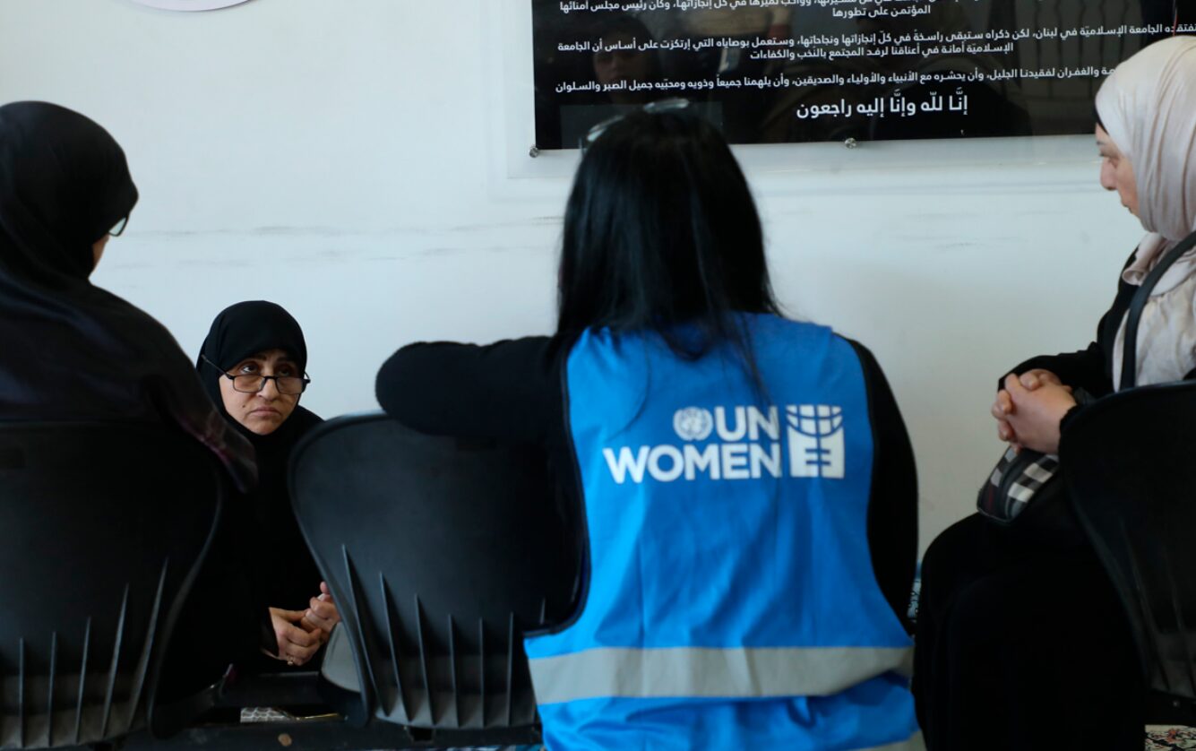 Eine Frau mit UN Women Weste spricht mit drei Frauen in einer Universität, die als Gemeinschaftsunterkunft für Geflüchtete umfunktioniert wurde. UN Women Nothilfe im Libanon.