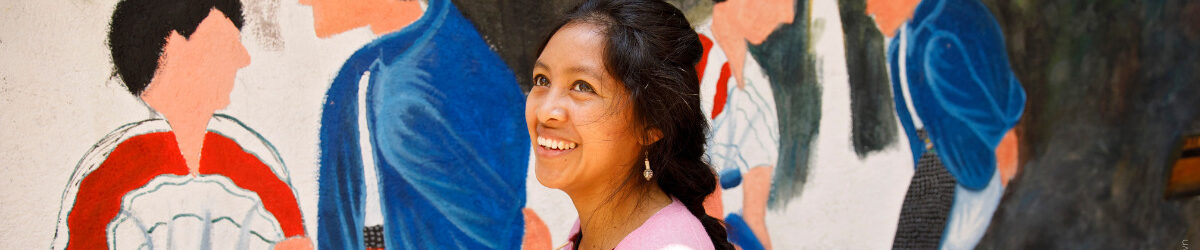 Lächelnde Frau vor mit Menschen bemalter Wand - Credit: UN Women/ Ryan Brown